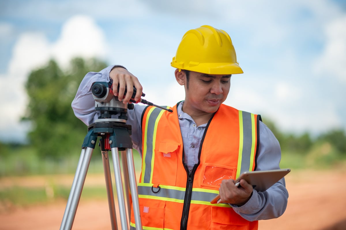 Land surveyors using a tripod theodolite to survey a plot of land in Uganda