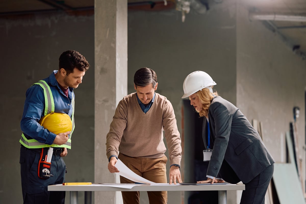 Building contractor cooperating with a worker and project manager while analyzing construction plans at building site