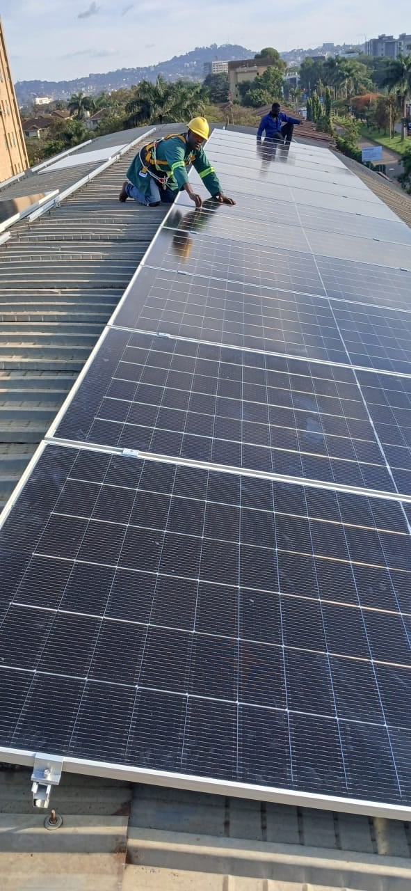Two workers installing solar panels on a rooftop with a cityscape and hills visible in the background