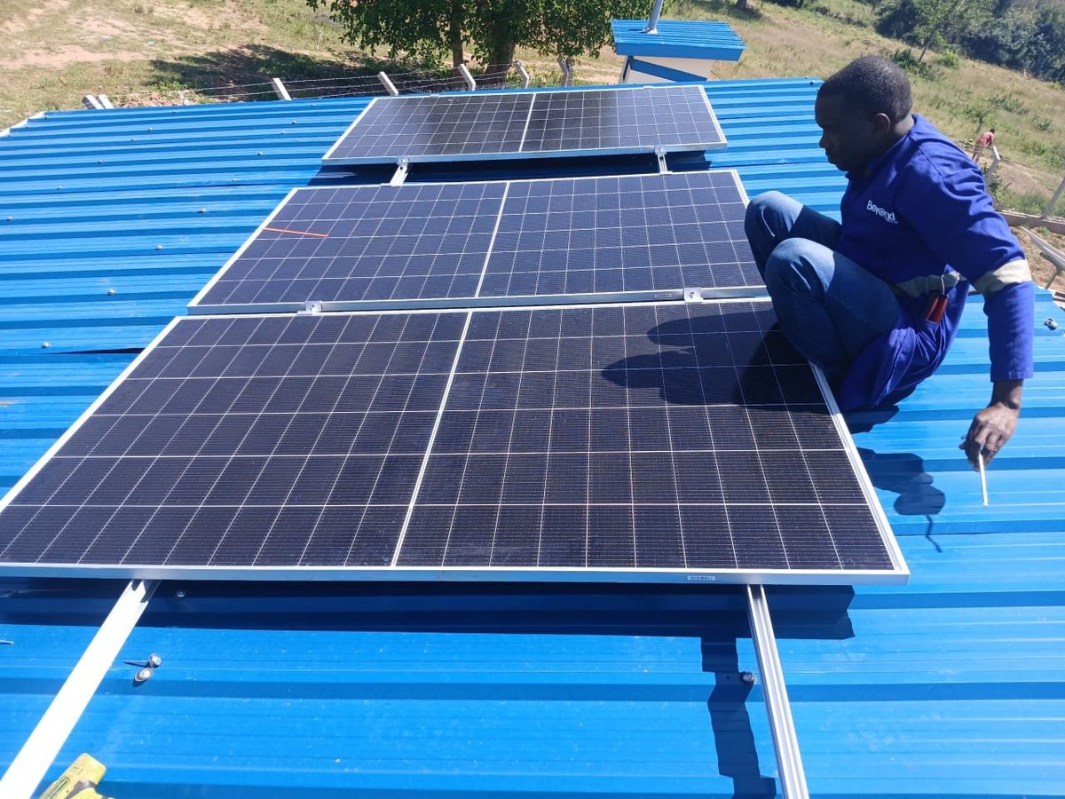 Technician installing solar panels on a bright blue metal roof in a rural area